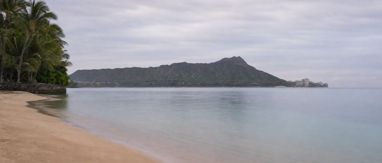 The south shore of Oʻahu on a calm overcast morning, with Diamond Head in the distance.